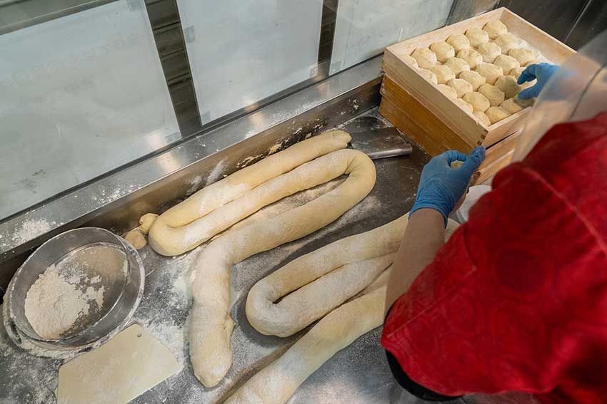 セントラルキッチンから届いた生地を手でこねた後、重さを測って小分けにし、二次発酵を行う