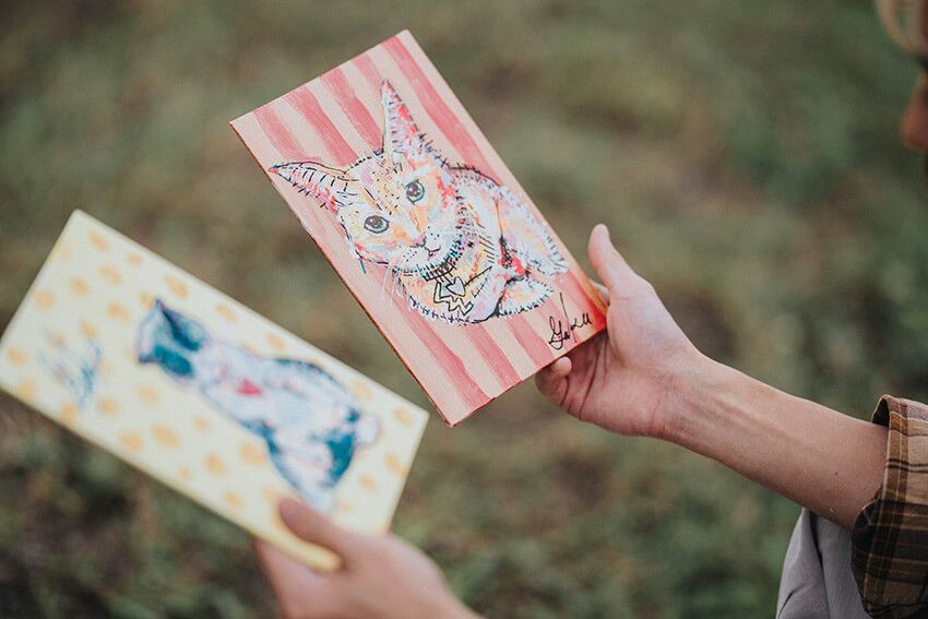 実家で暮らす猫をモデルに描いた一枚。ストライプの背景に映えるまっすぐな瞳と、「Lycka（幸せ）」という言葉が、日々のぬくもりを思い出させてくれる。