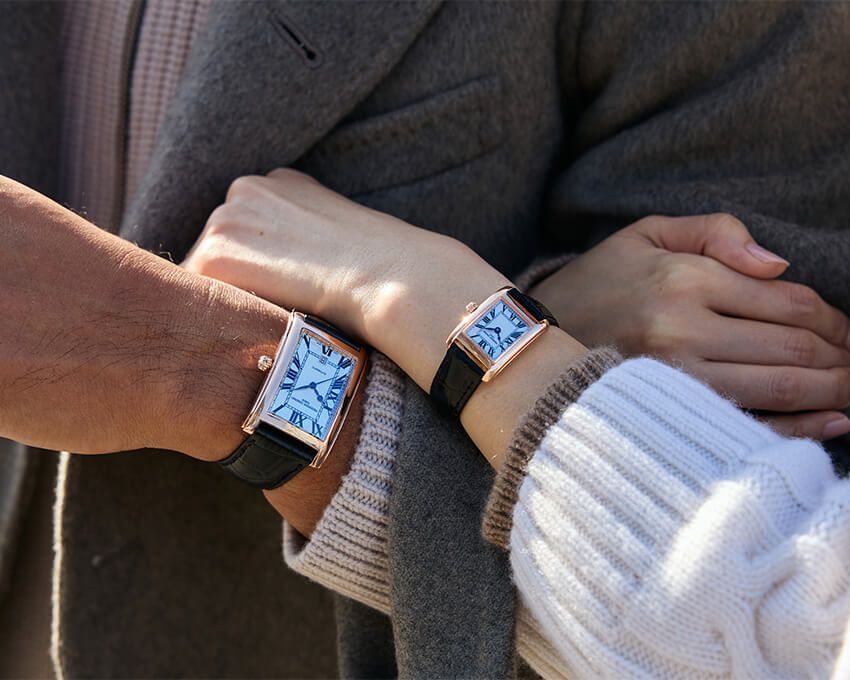 左は、メンズにふさわしい大ぶりの自動巻きモデル。右は小ぶりなクオーツモデル。ともに漂うアール・デコ調のムードが、ふたりの服装をリンクしてくれる。なお、メンズ・レディスともにオーソドックスなSSケースのタイプも展開。男性の腕時計は上の写真を参照。女性●「クラシック カレ オートマチック」SSケース（ローズゴールドプレート加工）、ケースサイズ縦23×横21㎜、クオーツ。20万3500円／フレデリック・コンスタント　0570-03-1988