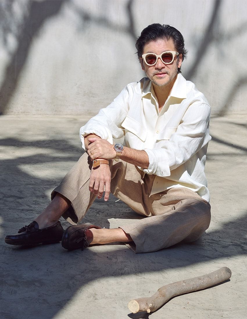オフホワイトのシャツとベージュのパンツは、ともにリネン素材。端正ななかに肩の力が抜けた佇まいから、静かにラグジュアリーが滲み出ている。長年愛用している私物のロエベのサングラスとスウォッチの腕時計も上品に馴染んでいる。シャツ12万9800円、パンツ10万6700円、靴参考商品／すべてラルフ ローレン パープル レーベル（ラルフ ローレン　0120-3274-20）