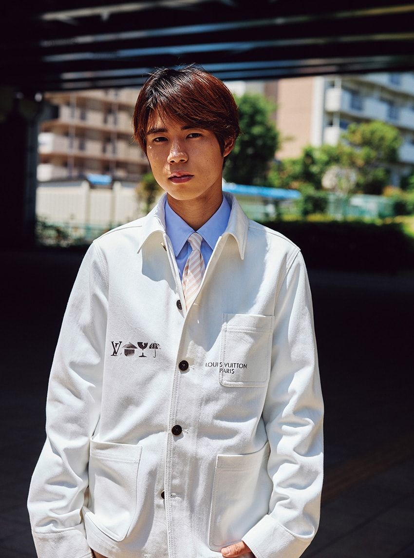 生成りのジャケットに、白×ベージュのレジメンタルを合わせた端正なスタイル。黒のステンシルロゴが程良いアクセントとなり、ワークウェア由来の武骨さとルイ・ヴィトンらしい洗練が静かに共存する。ジャケット42万4600円［予価］、シャツ18万4800円、タイ4万4000円／すべてルイ・ヴィトン